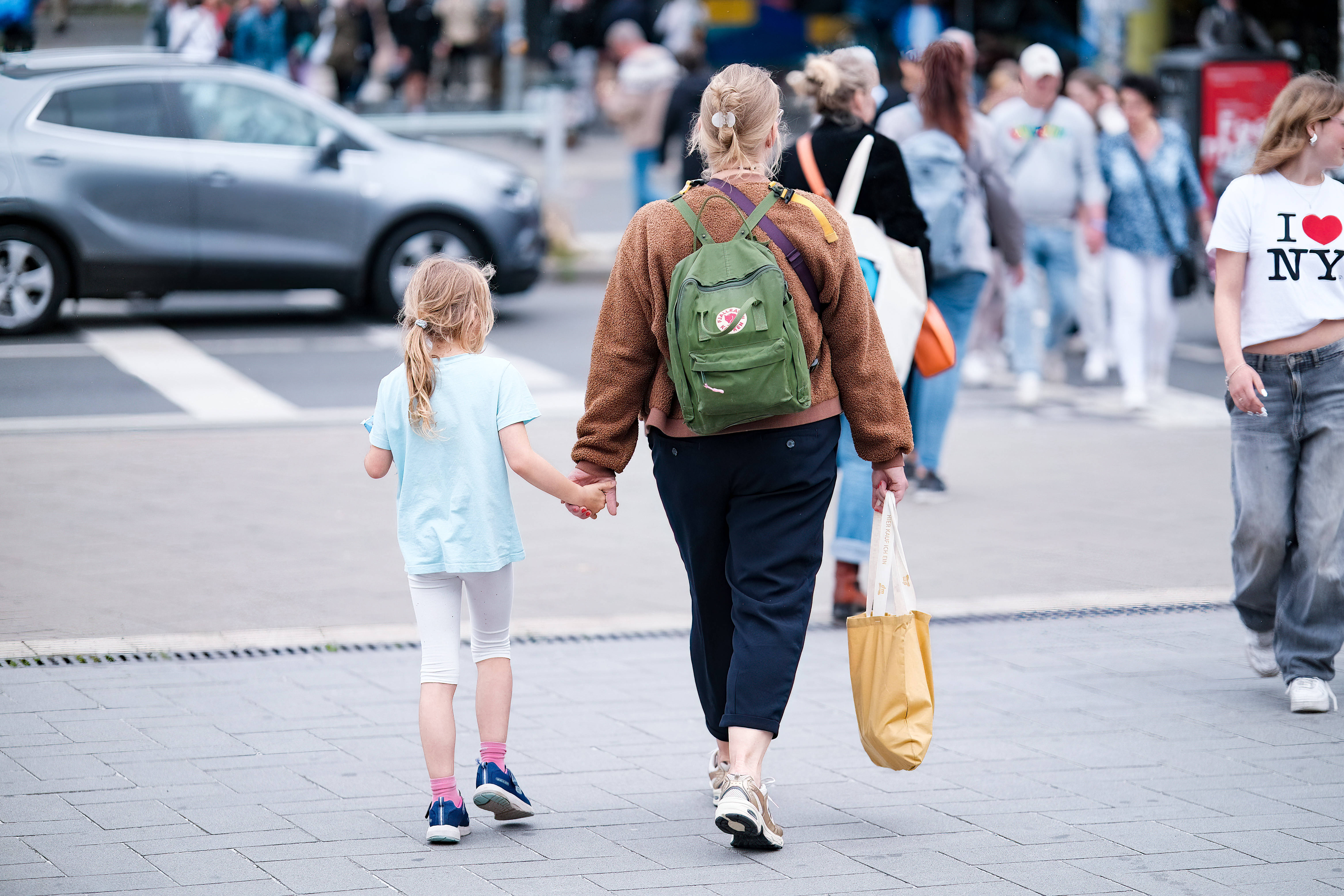 Ein Kind und eine Frau mit Einkaufstüte laufen durch eine Fußgängerzone