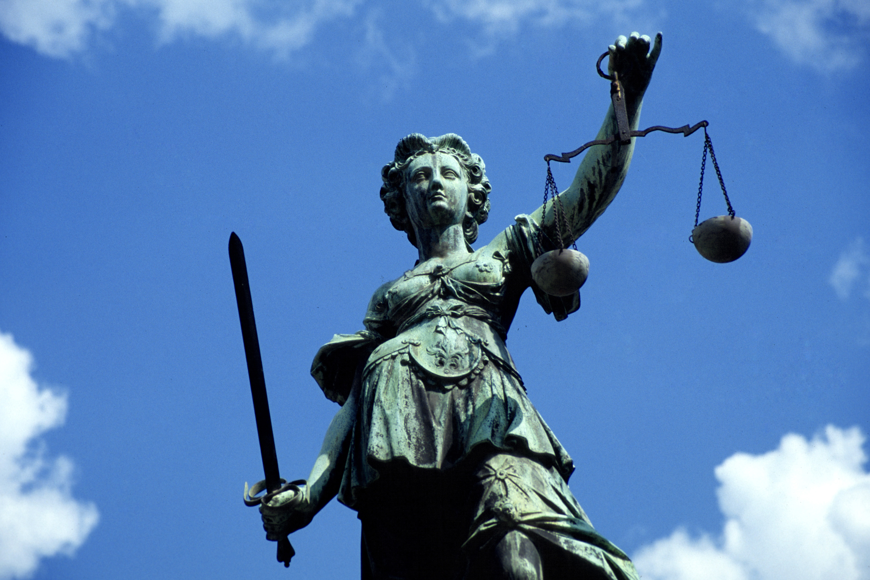 Eine Bronzestatue der Justizia steht vor blauem Himmel