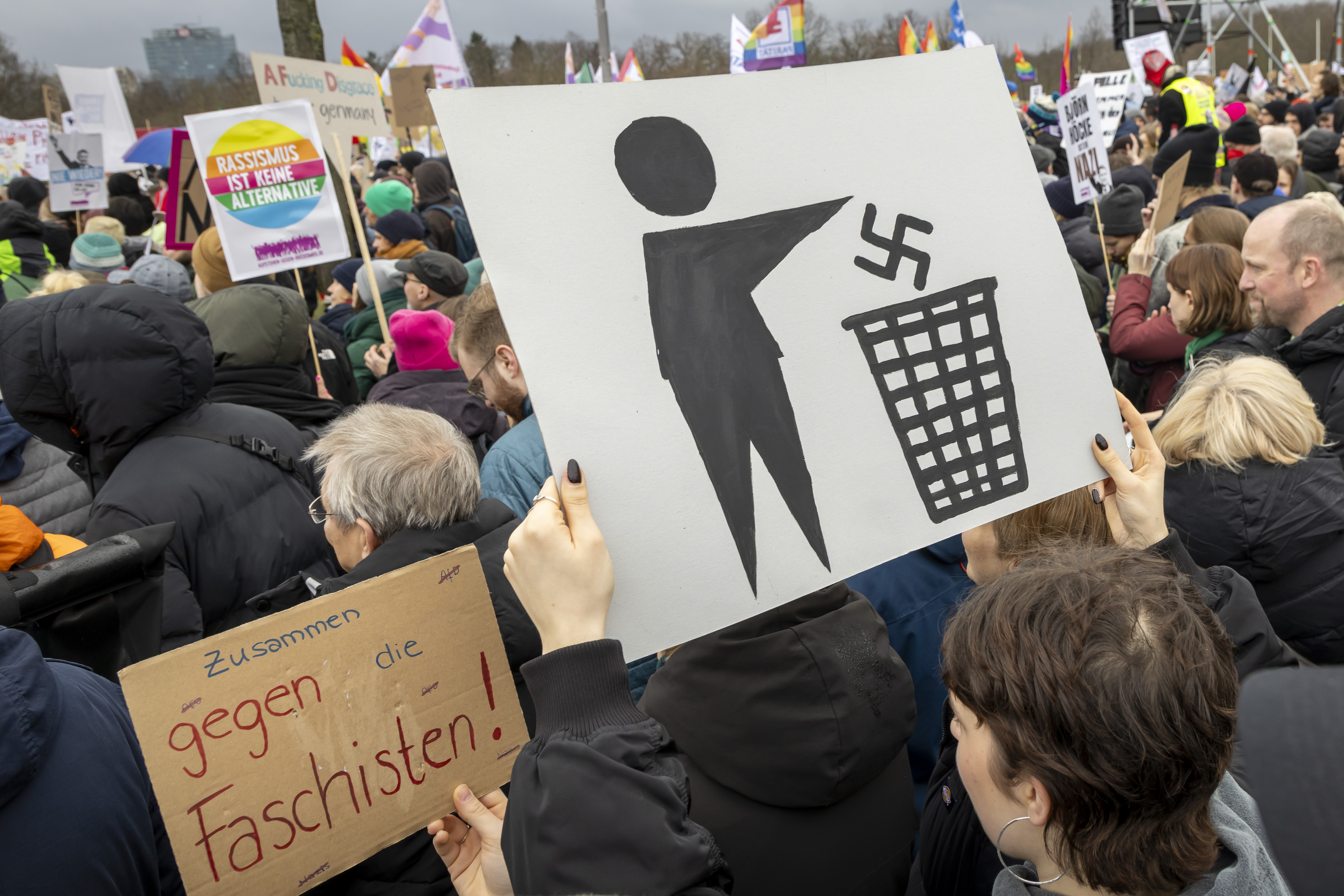 Blick auf Demonstranten und ein Schild, auf dem ein Hakenkreuz in den Papierkorb geworfen wird