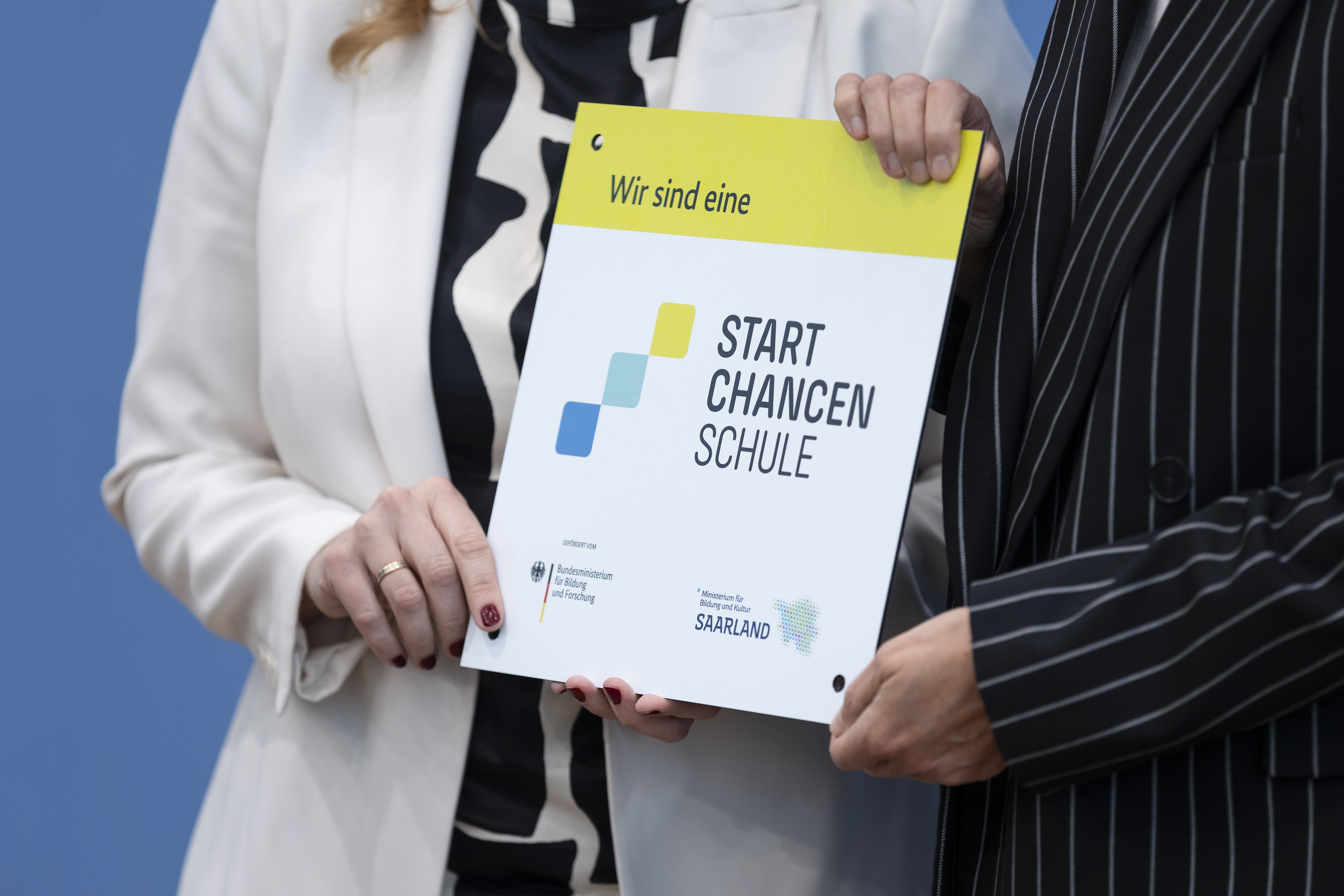 Vier Hände halten ein Schild mit Aufschrift „Startchancenschule” in die Kamera