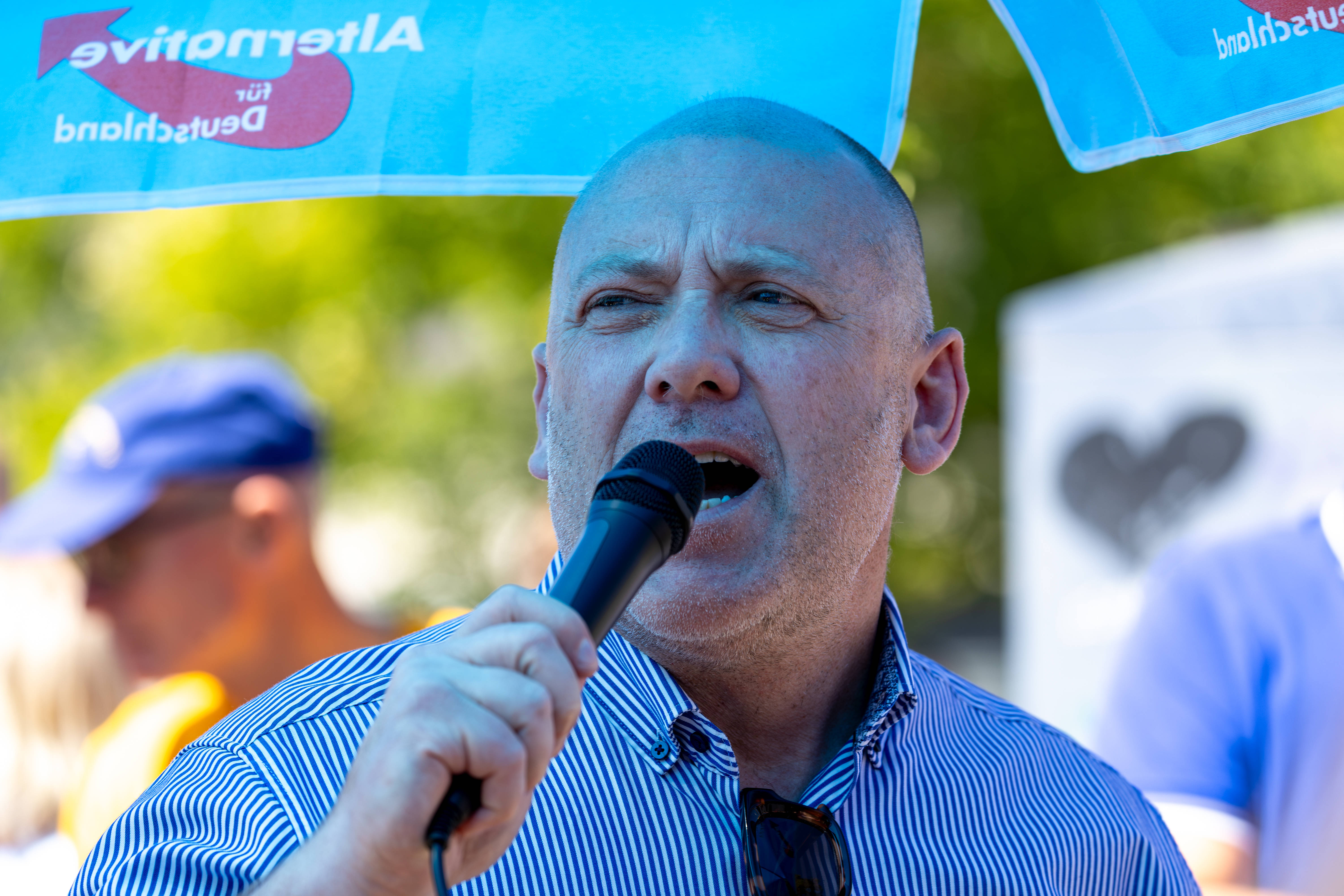 Joachim Paul mit Mikrofon unter einem blauen AfD-Schirm