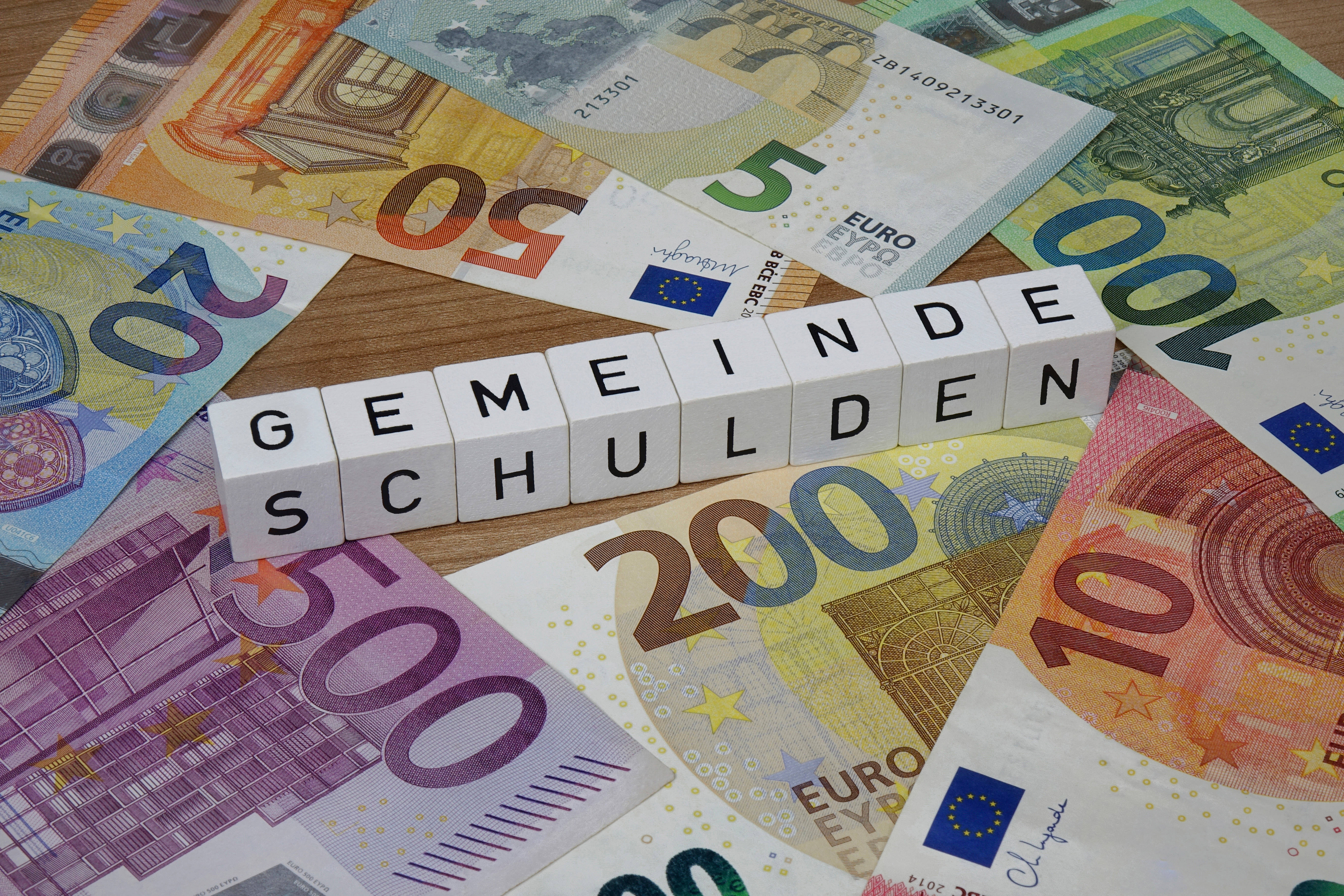 Geldscheine und Würfel mit Buchstaben, Aufschrift Gemeinde-Schulden